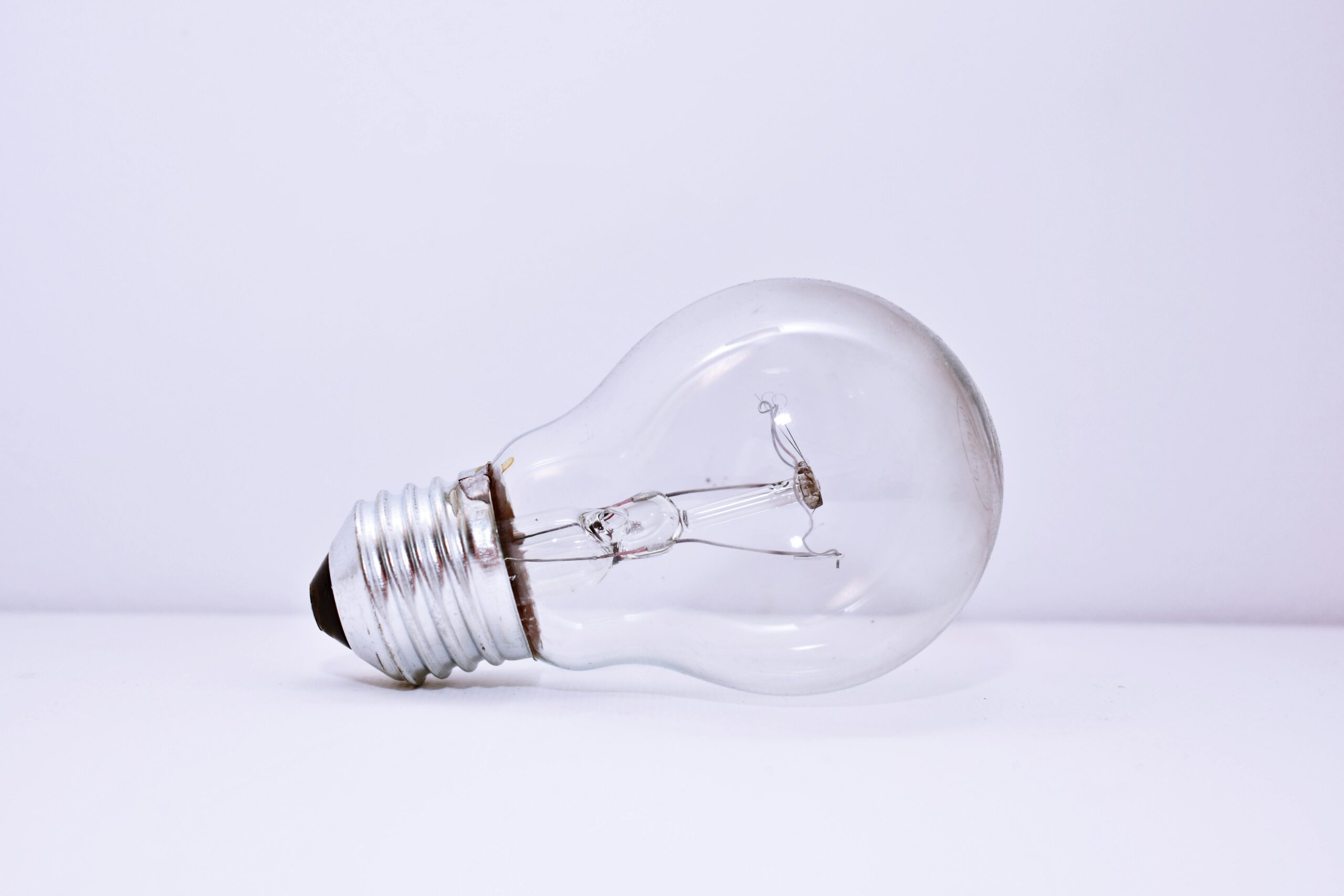 A clear incandescent light bulb lying on a simple white background, showcasing minimalism.